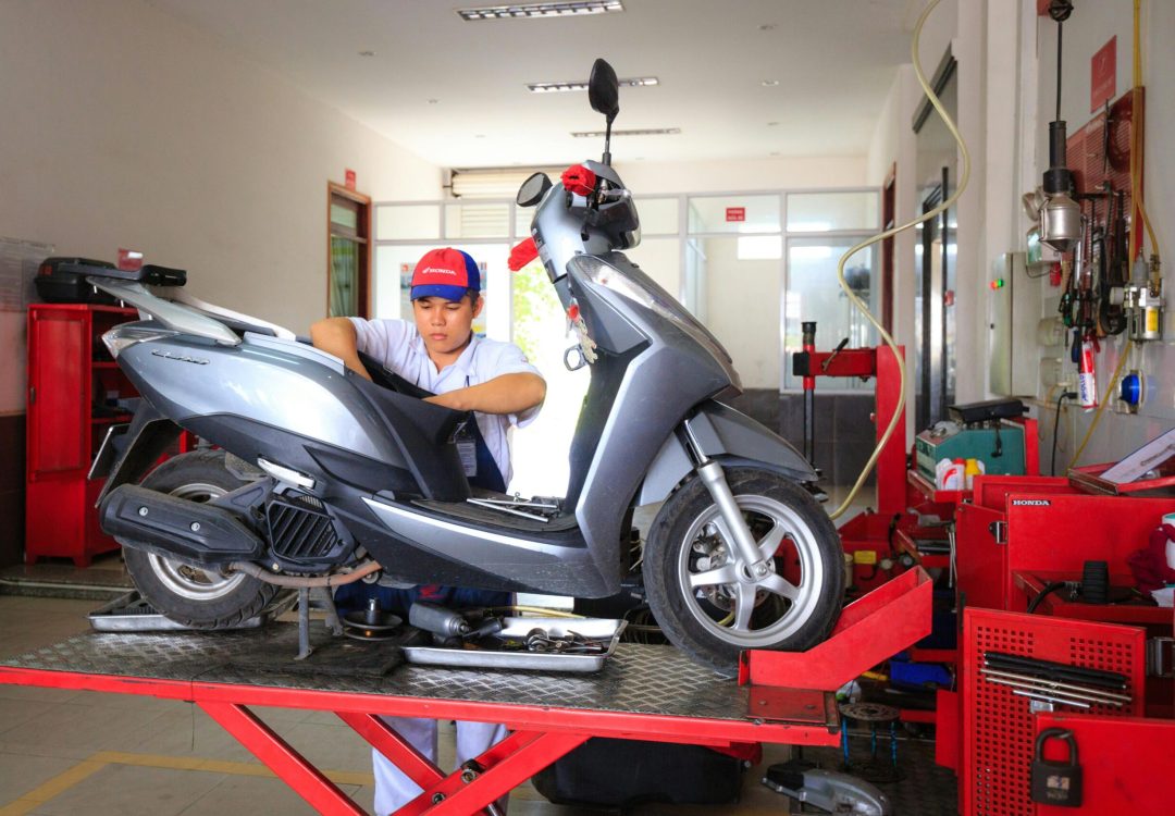 Mechanic working on a scooter in a well-equipped workshop, showcasing maintenance and repair services.